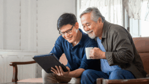 A young man points to the screen of a tablet while showing an older man something on the tablet.